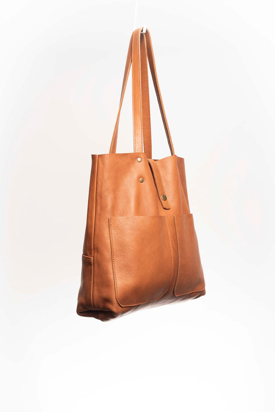 Leather Tote Bag, unlined hand bag. It features two open exterior pockets and one internal zippered pocket. It comes with fixed leather handles. It’s held shut by a sturdy snap closure.